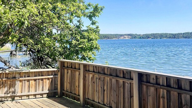 A wooden deck overlooking a calm lake with a clear sky. - 4 Person Holiday Home in Akersberga (Akersberga)