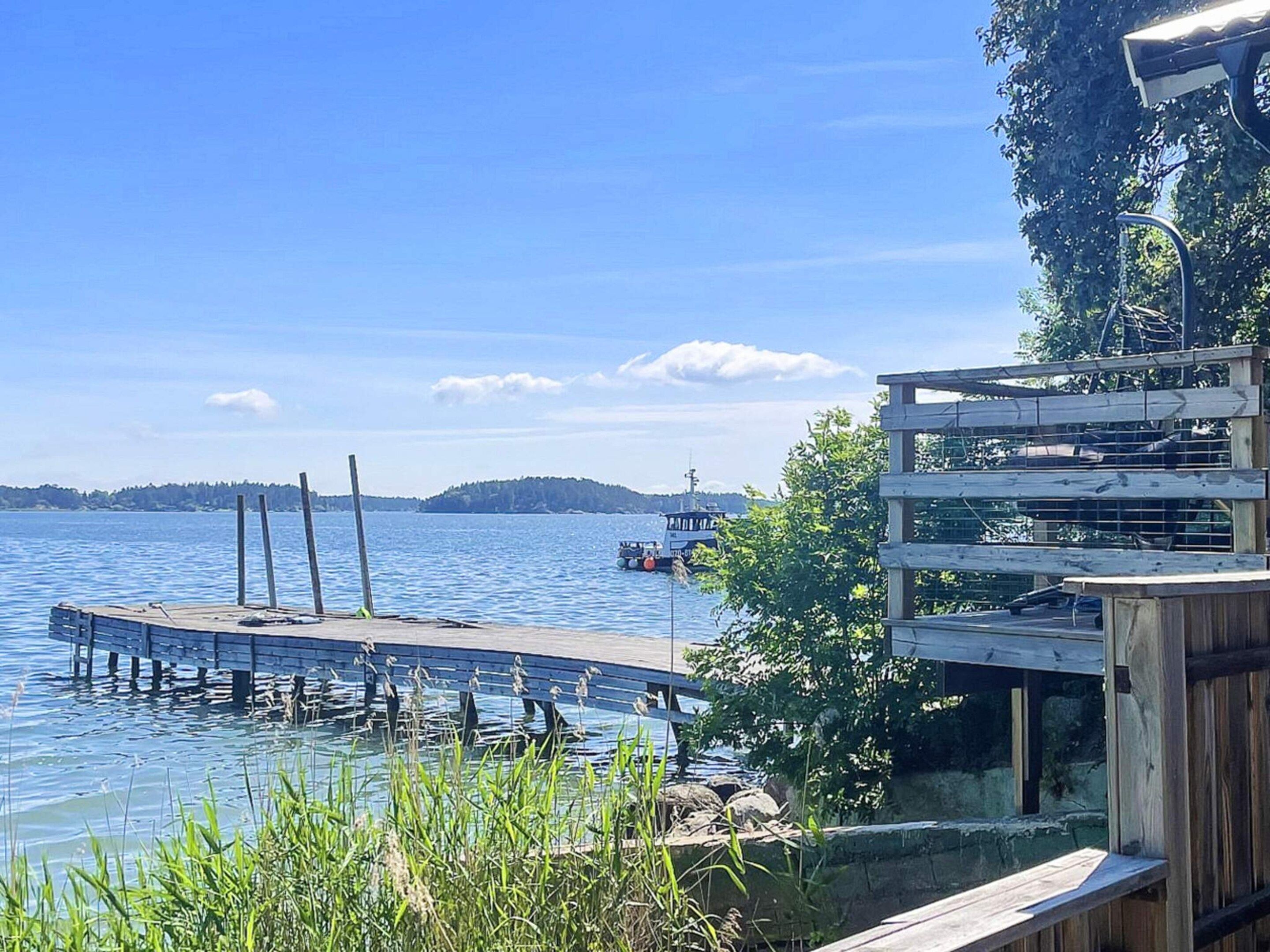 A wooden dock extending into a calm lake with a boat in the distance and a forested hill in the background.