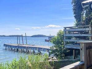 A wooden dock extending into a calm lake with a boat in the distance and a forested hill in the background. - 4 Person Holiday Home in Akersberga (Akersberga)