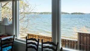 A room with a view of a lake, wooden deck outside, and two chairs with blue cushions. - 4 Person Holiday Home in Akersberga (Akersberga)