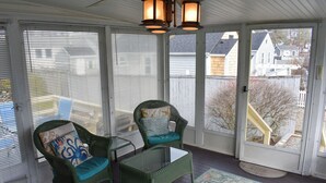 Eine überdachte Veranda mit Korbstühlen, einem Glastisch und einem gemusterten Teppich.