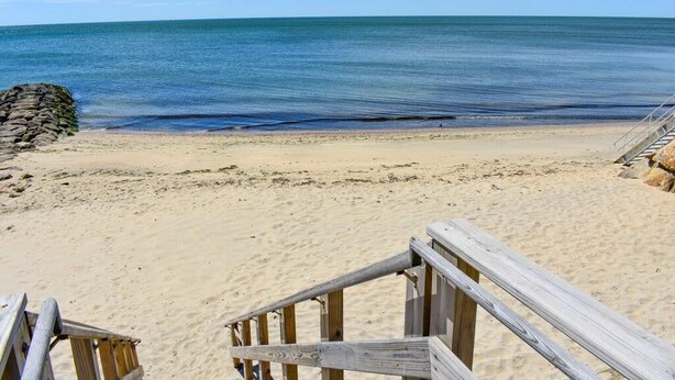 Ein sandiger Strand mit einer Holztreppe, die zum Wasser hinabführt.