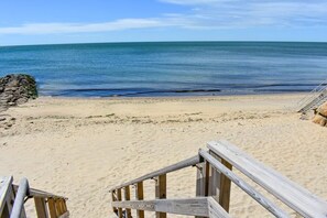 Una playa arenosa con una escalera de madera que baja hacia el agua.