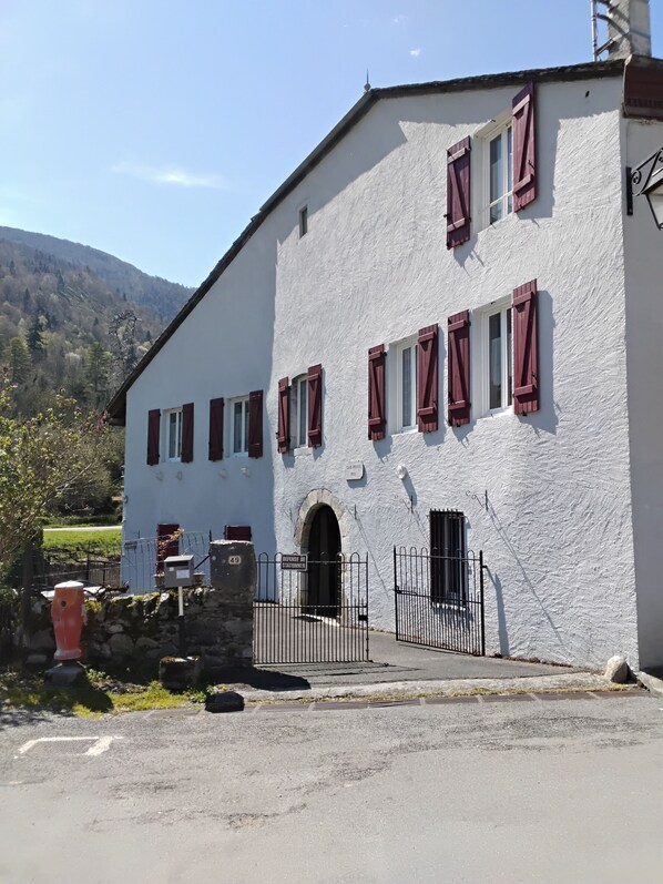 Un edificio blanco con contraventanas rojas, una pared de piedra y una reja de metal.