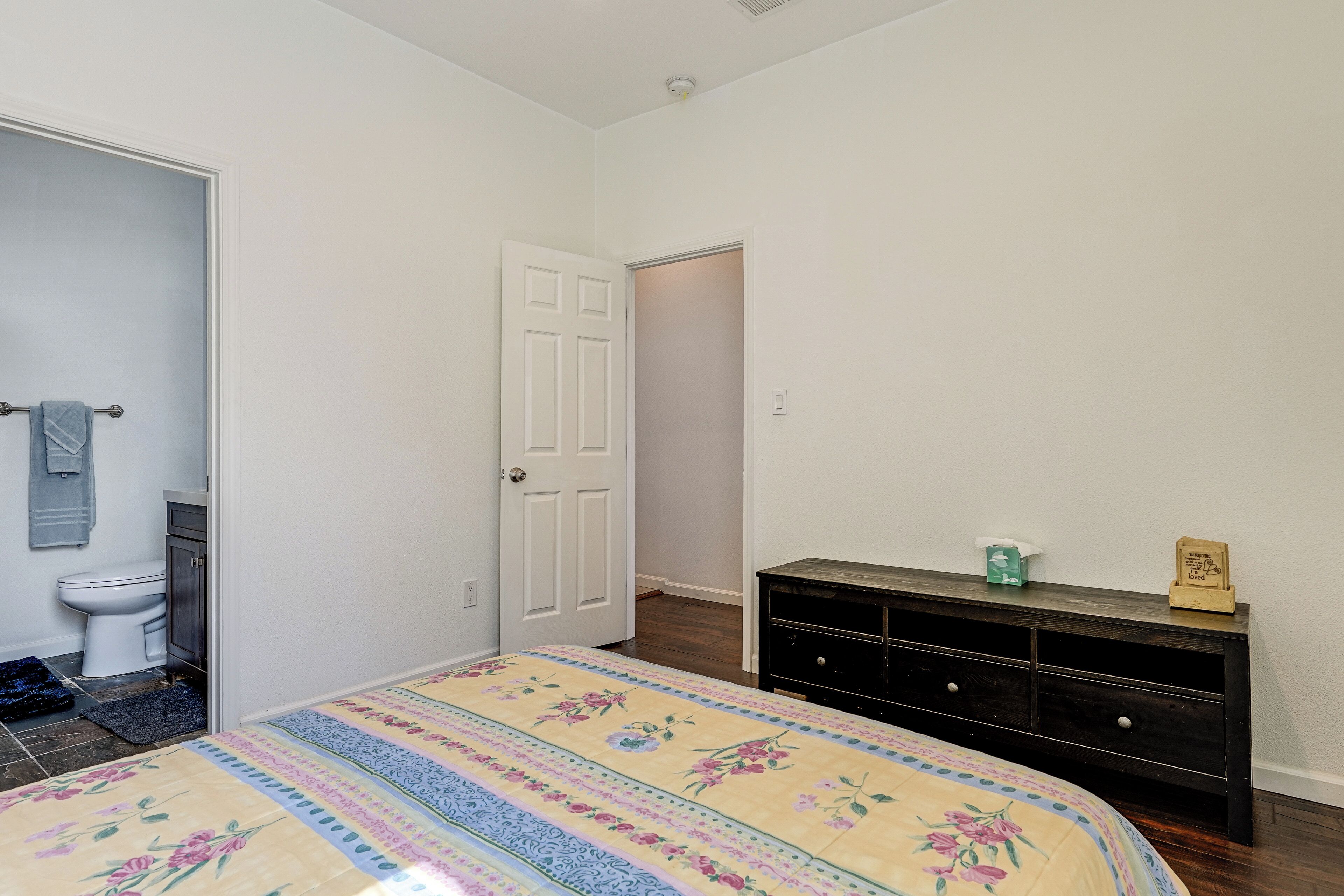 A bedroom with a bed, a dresser, a door, and a bathroom visible in the background.