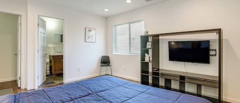 Ein Schlafzimmer mit einem Bett, einem an der Wand befestigten Fernseher und einer Tür zu einem Badezimmer.