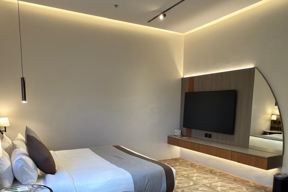 Una habitación de hotel moderna con cama, una mesa de centro redonda, televisor montado en la pared y piso estampado.