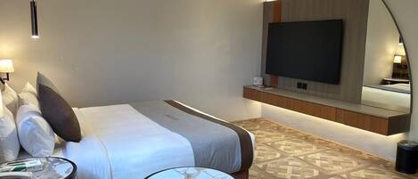 A modern hotel room with a bed, a round coffee table, a TV mounted on the wall, and a patterned floor.