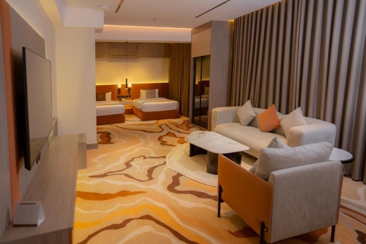 Una habitación de hotel con sofá, dos camas, televisión y alfombra estampada.