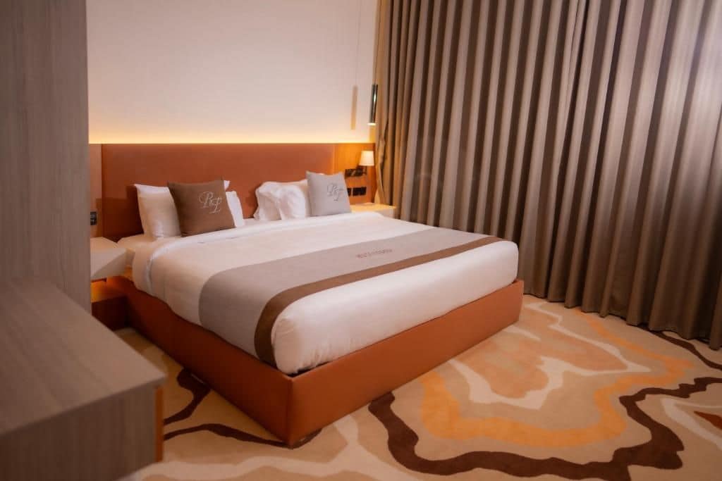 A hotel room with a large bed, a nightstand, a lamp, and a window with curtains.