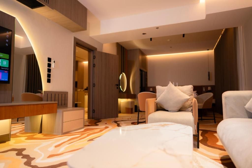 A modern hotel room with a flat-screen TV, a desk, a sofa, and a patterned carpet.
