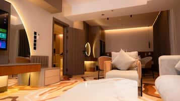 A modern hotel room with a flat-screen TV, a desk, a sofa, and a patterned carpet.