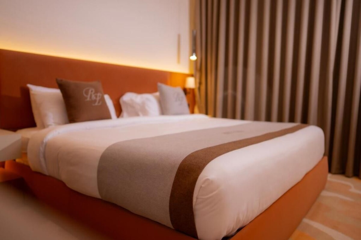 Una habitación de hotel con cama, almohadas, mesita de noche y una ventana con cortinas.