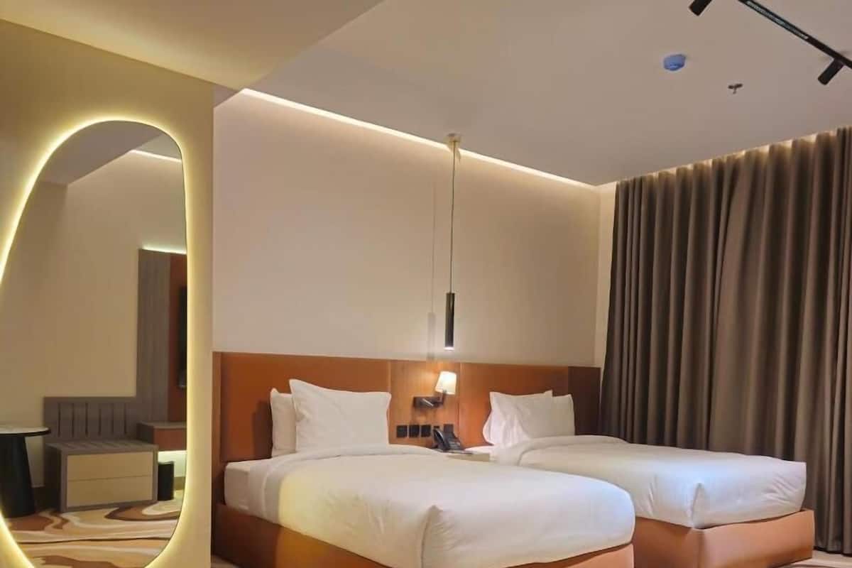 A hotel room with two beds, a round table, a mirror, and a modern light fixture.