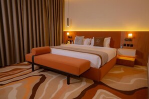 Habitación de hotel con una cama grande, un banco y una alfombra estampada.