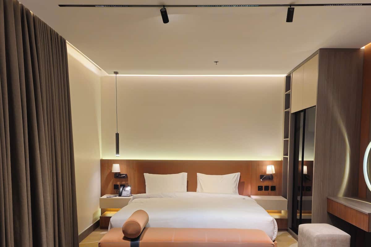 A hotel room with a bed, bedside tables, a lamp, a mirror, and a patterned carpet.