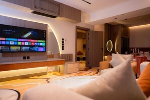 A modern hotel room with a flat-screen TV, a sofa, a dining table, and a circular light fixture.