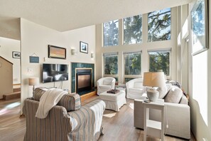Un salón amplio con chimenea, ventanas grandes y un televisor de pantalla plana.