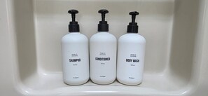 Drie witte flessen van Public Goods shampoo, conditioner en douchegel in een witte wasbak.