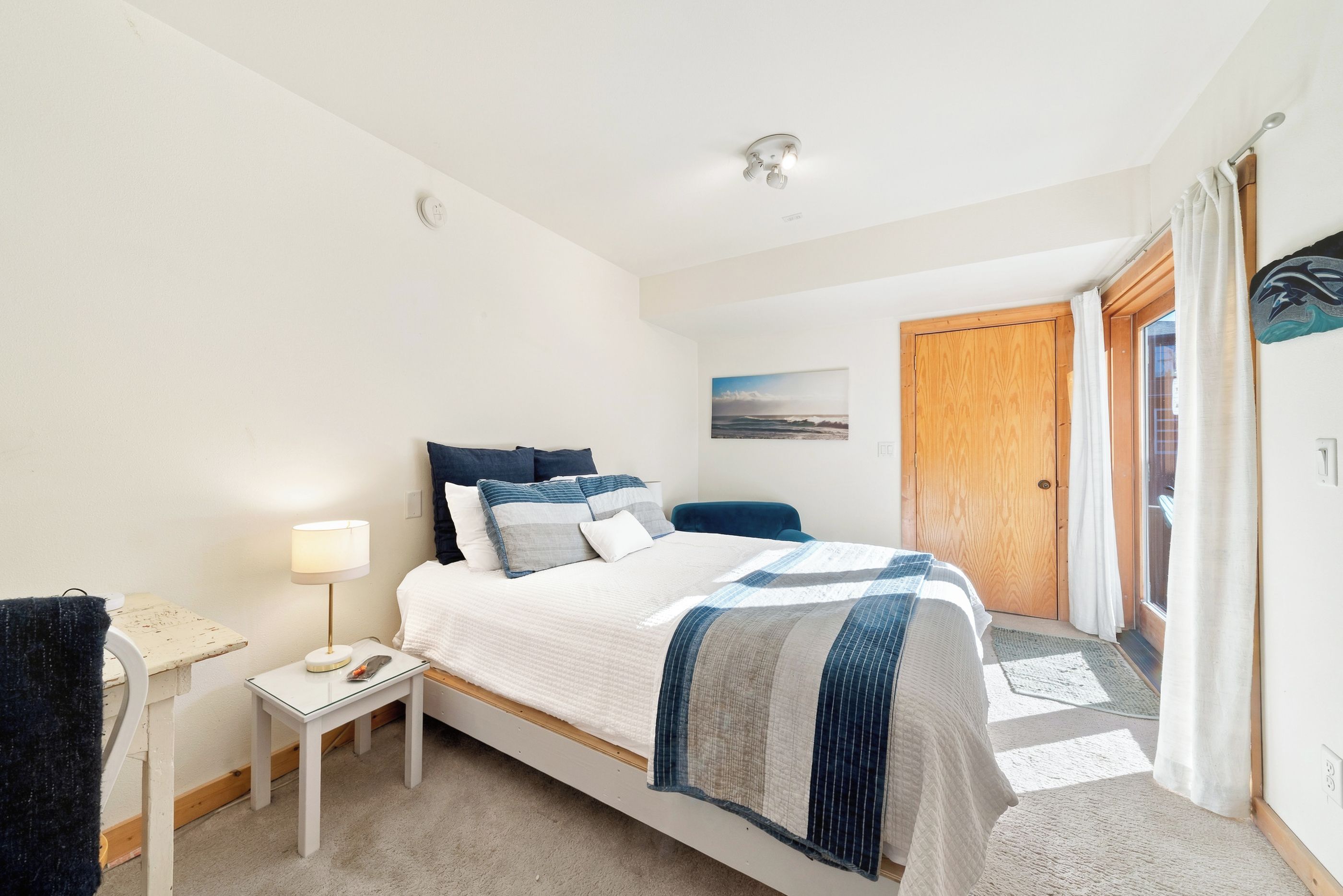 Relax and unwind in the bright, inviting main-level bedroom featuring a comfortable queen bed, cozy sitting area, and sliding glass doors that fill the space with natural light.