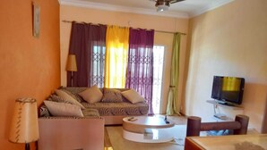 A living room with a sofa, a coffee table, a TV, and a bookshelf. - Private 3BR Villa & Pool | Flic en Flac | 100% Privacy & 7Mins walk to the beach (Flic en Flac)