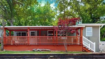 Une maison à deux étages avec une façade rouge, un porche doté d’une balustrade et un petit garage attenant.