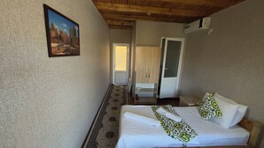 A bedroom with a bed, a painting on the wall, a wardrobe, and a door leading to another room.