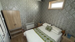 A bedroom with a bed, a wardrobe, a radiator, a nightstand, and a window.
