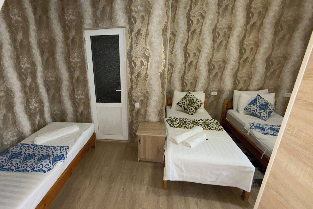 Ein Zimmer mit zwei Einzelbetten, einem kleinen Nachttisch, einer Tür und einer strukturierten Wand.