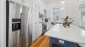 Una cucina moderna con elettrodomestici in acciaio inossidabile, mobili bianchi, un'isola in marmo e una lampada a sospensione.