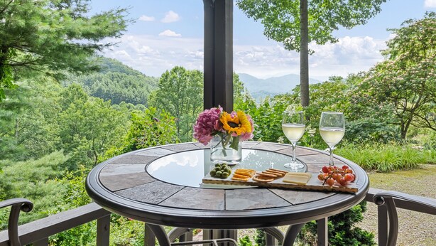 A round glass table with a view of a mountainous landscape, a vase with flowers, and a glass of white wine. - Peaceful Mountain Hideaway with a view, near Maggie Valley and Asheville (Waynesville)