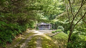 A house with a porch, surrounded by dense greenery and a gravel path leading to it. - Peaceful Mountain Hideaway with a view, near Maggie Valley and Asheville (Waynesville)