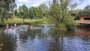 Una zona lungo il fiume con persone a cavallo e in acqua, circondata da alberi e una struttura in legno.