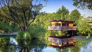 Una struttura in legno a più livelli con una superficie d'acqua riflettente, circondata da alberi.
