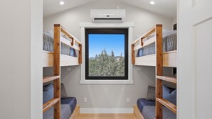 Een kamer met stapelbedden, een raam met uitzicht op een bos, een airconditioning en een houten vloer.