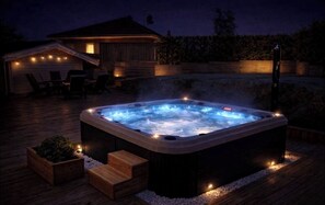 Un bain à remous sur une terrasse en bois, avec un espace salon couvert et un bâtiment en arrière-plan.