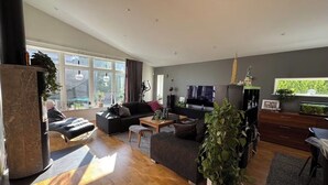 Ein modernes Wohnzimmer mit einer Couch, einem Couchtisch und einem Fernseher. Ein großes Fenster und eine Pflanze stehen in der Ecke.