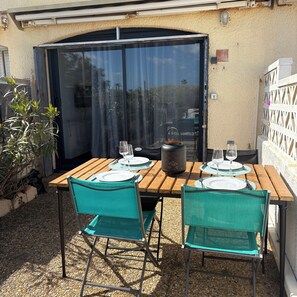 An outdoor patio with a table set for two, a grill, and a sliding glass door. - Appart. Seafront 1 to 4 pers. Village Le Barcares, Swimming pool, Everything on foot! (Le Barcarès)