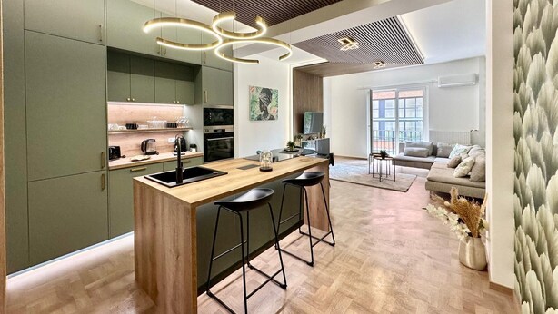 Una cucina moderna con isola centrale, sgabelli da bar e zona pranzo con divano.