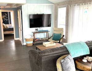A living room with a sofa, a television, a small table, a chair, and a basket. - 4th NIGHT FREE @The Shell Shack - A Bayside Retreat! (Jamaica Beach)