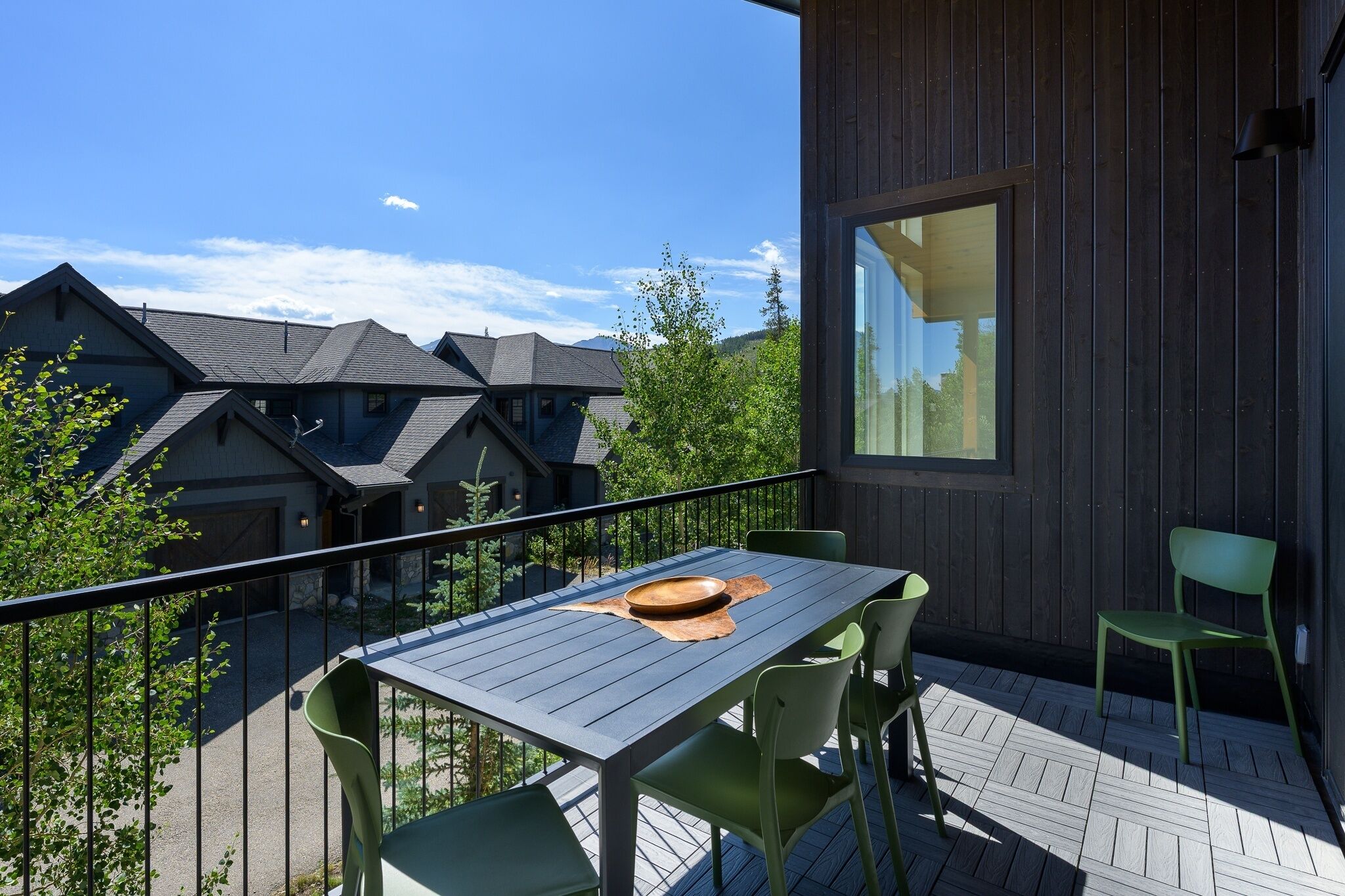A balcony with a table and chairs, a wooden deck, and a view of neighboring houses.