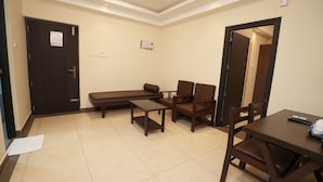 A room with a sofa, two chairs, a table, a door, and an air conditioning unit. - Krishna Royal Club (Guruvayur)