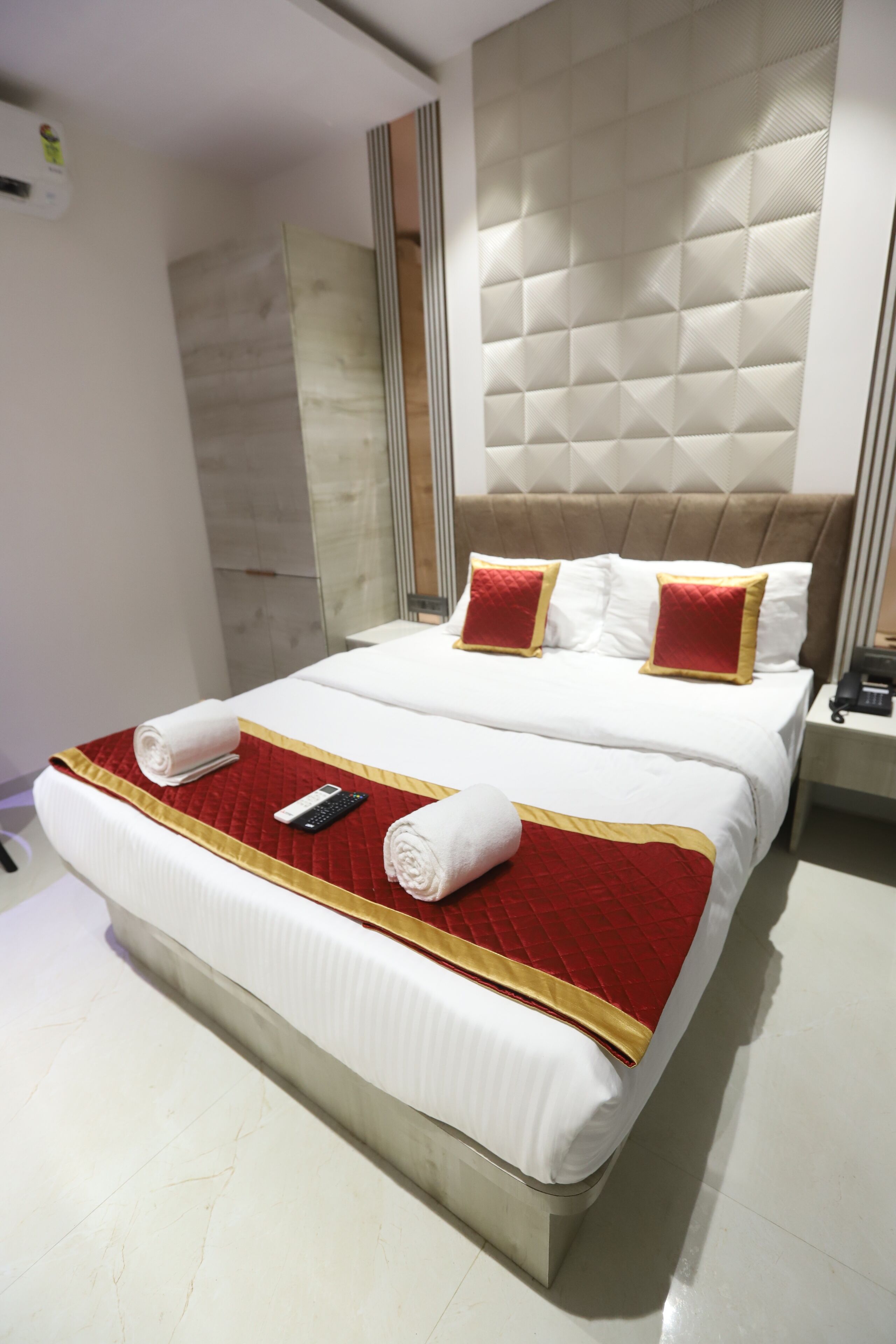 A hotel room with a large bed, a bedside table with a phone, and a wall-mounted air conditioning unit.