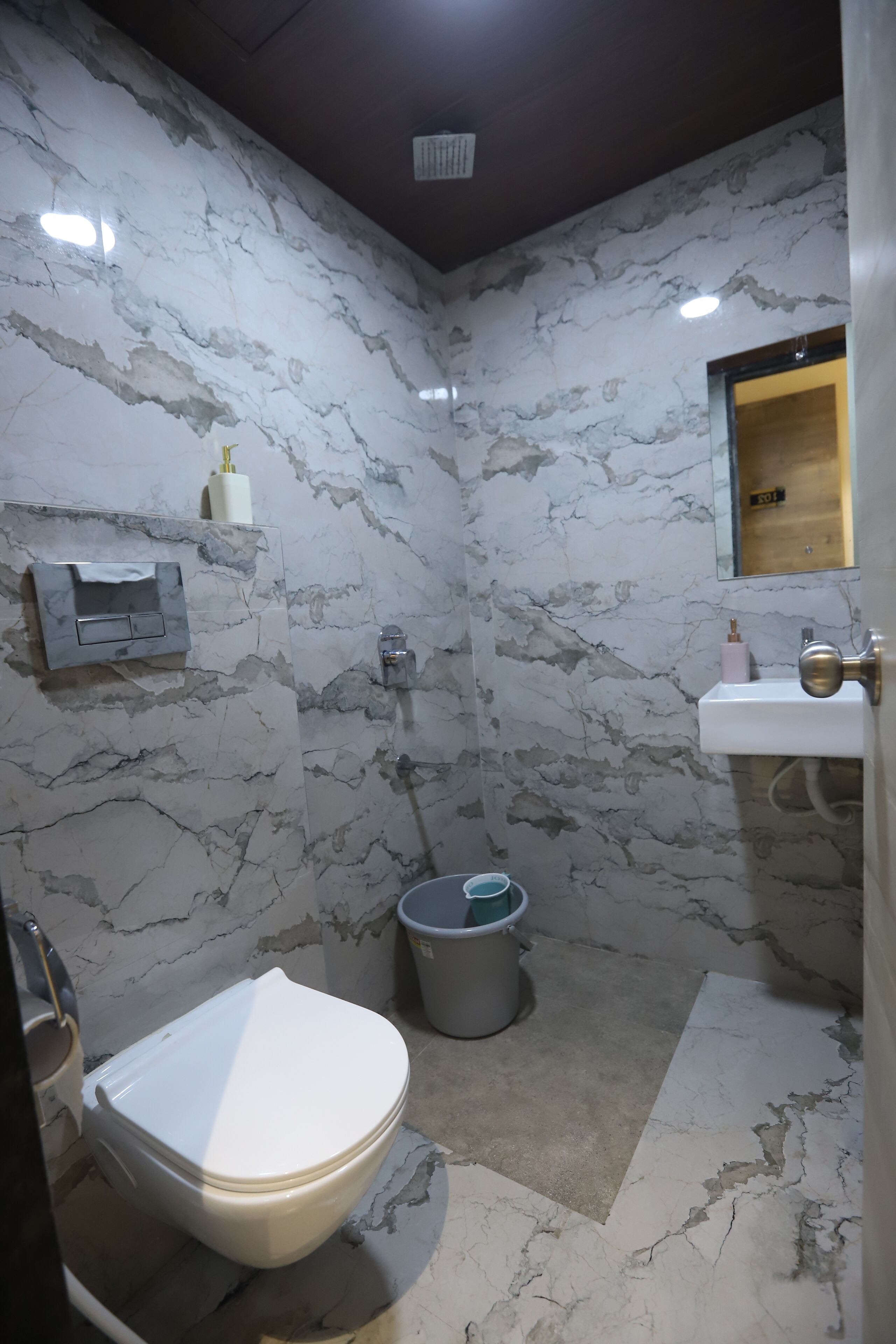 Une salle de bain avec un mur en marbre, des toilettes, un lavabo et une douche.