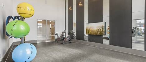 Un gimnasio con pelotas de ejercicio, bicicletas estáticas y una pantalla de televisión grande.