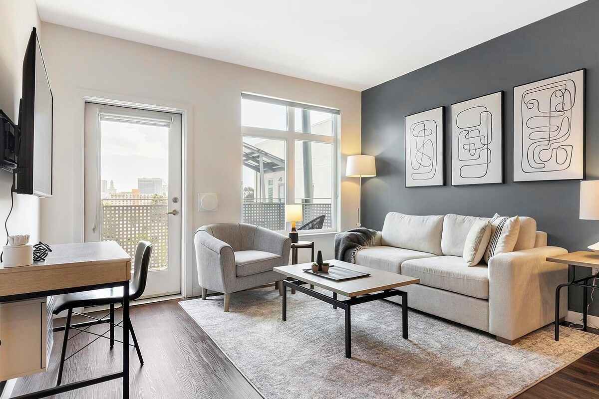 A modern living room with a sofa, armchairs, a coffee table, and a TV. There are three wall-mounted artworks and two floor lamps.