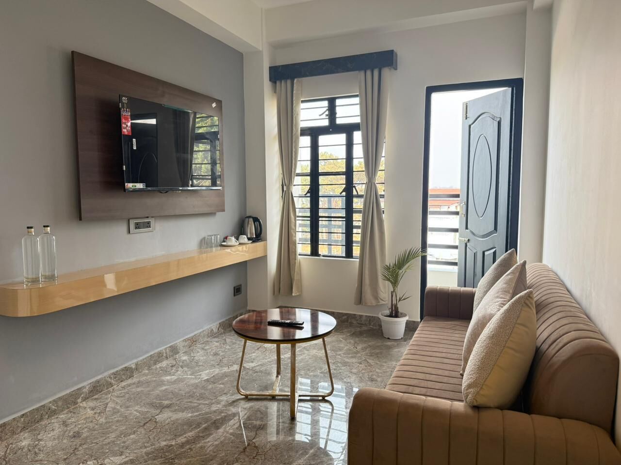 Una sala de estar con un televisor montado en la pared, un sofá, una mesa de centro y una ventana con cortinas.