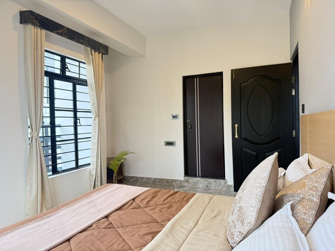 A bedroom with a bed, a window with curtains, a door, and a plant.