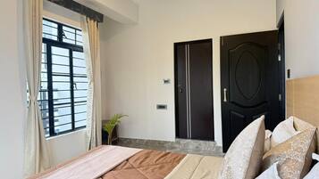 A bedroom with a bed, a window with curtains, a door, and a plant.