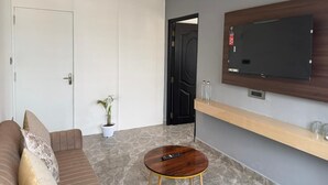Un soggiorno moderno con un divano, un tavolino da caffè, una TV a parete e una porta che dà su un'altra stanza.